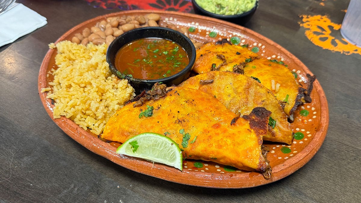 Quesa Birria Tacos plate with a cup of consomé
