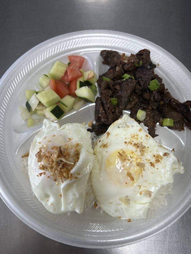 Beef tapa plate with two sunny-side-up eggs over garlic rice and a cucumber-tomato side