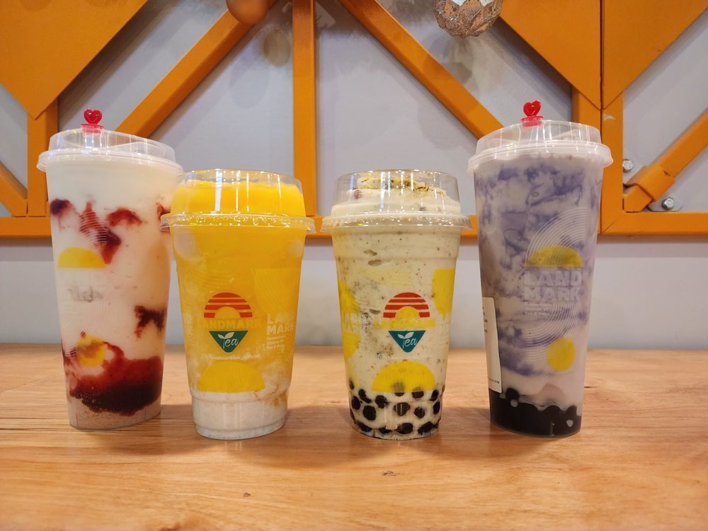 Four Landmark Tea drinks, including a mango sticky rice slushy and milk teas, lined up on the counter in front of the cafe's mango-yellow geometric wall